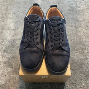 Mörkblåa sneakers från Christian Louboutin - Snygga svarta sneakers i mocka från Christian Louboutin med den ikoniska röda sulan. Skorna har snörning och en stilren design som passar perfekt för en trendig look. Se bild fyra för defekt och kommer med allt.