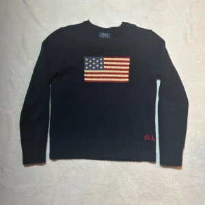 Mörkblå stickad tröja från Ralph Lauren - Säljer en snygg mörkblå stickad tröja från Ralph Lauren med en amerikansk flagga på bröstet. Tröjan har långa ärmar och en klassisk rund halsringning. Perfekt för en stilren och avslappnad look. Jag säljer varan eftersom de inte passar mig längre. Tröjan är i bra skick och har få spår av användning 