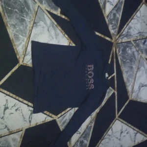 Svart långärmad tröja från Hugo Boss - Säljer en stilren svart långärmad tröja från Hugo Boss. Perfekt för en avslappnad men ändå elegant look. Tröjan har en klassisk design med märkets logotyp tryckt på framsidan.