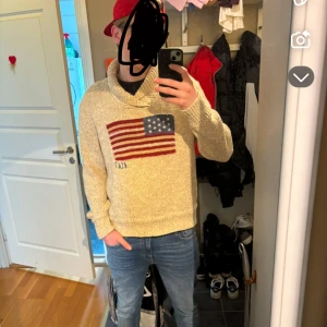 Ralph lauren tröja - Säljer en beige tröja från Ralph Lauren med en stor amerikansk flagga på framsidan. Tröjan har en hög krage och långa ärmar, perfekt för kyligare dagar. Den är både stilren och bekväm.