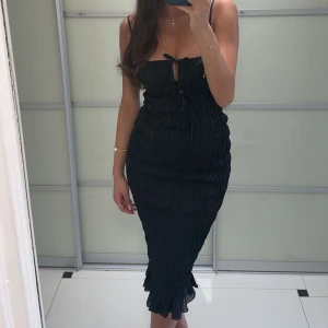 Svart axelbandslös klänning - Snygg svart axelbandslös klänning med knytning framtill och volangdetaljer vid fållen. Klänningen har en tight passform som framhäver figuren. Perfekt till mösspåtagningen. Klänningen sitter perfekt på mig som vanligtvis har 36/S, men skulle säga att den även passar 38/M då den är väldigt stretchig! Endas använd 1 gång och finns inga defekter 🩷