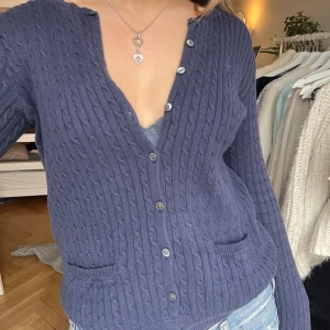 Mörkblå kofta från Ralph Lauren - Säljer denna snygga mörkblå kofta från Ralph Lauren med kabelstickat mönster. Koftan har knappar och små fickor framtill samt loggan på bröstet💙Enda tecknet på användning är att den släppt lite där bak vilket går att laga väldigt lätt! 🫶🪽