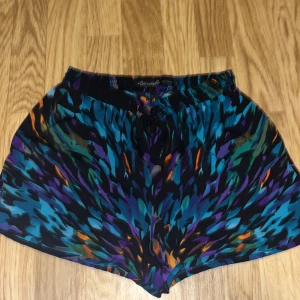 Färgglada shorts från BlendShe - Snygga och färgglada shorts från BlendShe med ett unikt mönster i blått, lila och orange. Perfekta för en somrig look. De har en bekväm passform med elastisk midja och knytband framtill.