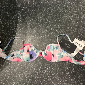 Flerfärgad bikiniöverdel från NA-KD - Trendig bikiniöverdel från NA-KD i en fkn mix av rosa, blå och vita nyanser. Säljer då den enligt mig var något liten i storleken. Den har en bygel för extra stöd och smala axelband. Perfekt för en solig sommardag💓💓Kan mötas upp i Halmstad!