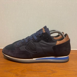 Mörkblåa philippe model - Snygga mörkblå sneakers med bruna detaljer från philippe model . Skorna har en kombination av mocka och skinnmaterial. Skorna är enkla att styla  och passar dig som har storlek 42. Skicket är nytt utan defekter. Priset kan diskuteras vid snabb affär 