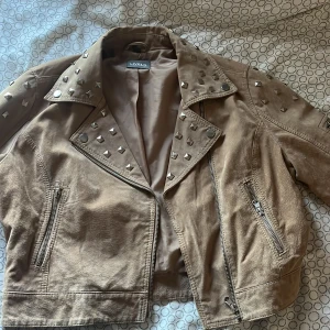 Beige skinnjacka från Livelo - Snygg beige skinnjacka från Livelo med coola nitar på axlarna och kragen. Jackan har dragkedja framtill och två fickor med dragkedjor. Perfekt för att ge din outfit en edgy touch! Använd 2-3 gånger💕 köpte för 1200kr på loppis i Stockholm🩷