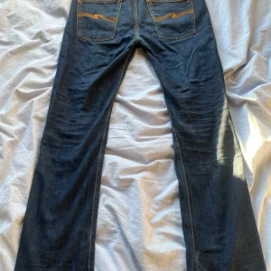 Mörkblå jeans från Nudie Jeans - Snygga mörkblå jeans från Nudie Jeans med klassisk femficksdesign och kontrasterande sömmar. De har en knappgylf och är tillverkade i slitstarkt denim. Perfekta för en avslappnad stil. Storlek W 30 L 32. Pris kan diskuteras😄