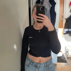 Svart långärmad topp från Stronger - Säljer en svart långärmad topp från Stronger. Toppen har en stilren design med texten 'STRONGER' tryckt på bröstet. Den är croppad och har en twistdetalj framtill som ger en snygg look. Perfekt för en casual outfit eller träning. 🖤