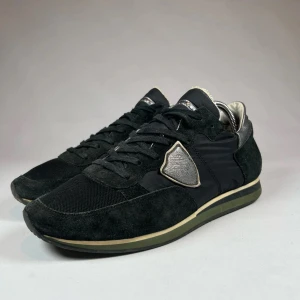 Svarta Philipe modell sneakers med silverdetaljer - Snygga svarta philipe modell sneakers med silverdetaljer och snörning. Skorna har en kombination av mocka och syntetmaterial, vilket ger dem en stilren look. Perfekta för en casual stil med en touch av elegans.