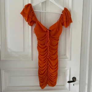 Orange klänning med drapering - Snygg orange klänning med volanger och rynkdetaljer. Den har korta ärmar och en knytning framtill som ger en fin passform. Perfekt för en färgglad look! 🧡