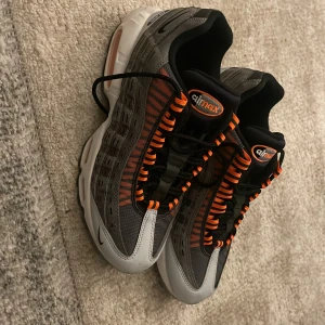 Nike Air Max sneakers i grå och orange - Snygga Nike Air Max sneakers i grått med orangea detaljer och svart snörning. Skorna har en unik design med synlig luftdämpning i sulan för extra komfort. Perfekta för en sportig look.