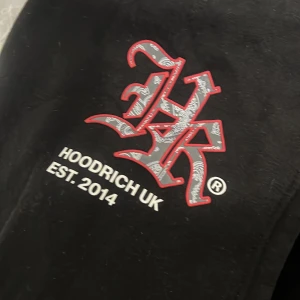 Svart hoodie från Hoodrich - Säljer en svart hoodie från Hoodrich med stor logga i vitt och rött på . Hoodien har en stor ficka framtill och är perfekt för en avslappnad stil. Märket är etablerat 2014 och ger en urban känsla. Kvitto finns och allt byxorna och hoodie.