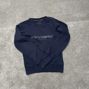 Mörkblå sweatshirt från Acqua Limone - Säljer en snygg mörkblå sweatshirt från Acqua Limone med tryck både fram och bak. Tröjan har långa ärmar och ribbade muddar vid ärmslut och nederkant. Perfekt för en avslappnad stil.