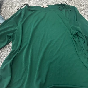 Grön topp från H&M - Säljer en stilren grön topp från H&M. Toppen har en enkel design med långa ärmar och en rund halsringning. 
