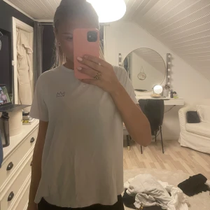 Vit t-shirt med blå text - Säljer en vit t-shirt med en cool blå krona på framsidan och texten 'CALLER BUDDY' på baksidan. Texten på baksidan säger 'Vi Jobbar Bara Varma Kunder' och har ett telefonnummer samt 'STOCKHOLM, SWEDEN'. 😇 Den är från Hov1 merchs hemsida 🥰 