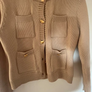 Stickad kofta från Zara - Beige stickad kofta från Zara med guldiga knappar. Köpt våren 2024 men finns inte kvar på hemsidan. Mycket bra skick.