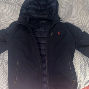 Varm polo ralph lauren höstjacka - Foderad skön Ralph lauren jacka med justerbar luva✅, justerbar midja✅ effektiva fickor med dragkedja samt innerficka✅ Defekt förekommer(lagning på insidan se bild 4) På utsidan är jackan till synes nyskick! Denna mångsidiga snygga jacka är ett KAP!