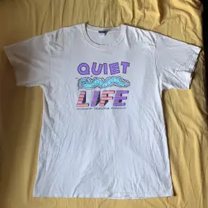 Säljer den här coola tröjan åt min kille. T-shirt från The Quiet Life i storlek L. Den har ett coolt tryck på framsidan med texten 'QUIET LIFE' i lila och rosa, samt en tecknad mask i turkos. Den har en liten fläck (se sista bilden).