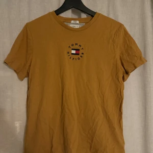 Gul t-shirt från Tommy Hilfiger - En fin gul/brun T-shirt från Tommy hilfiger i väldigt bra skick! 