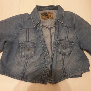 Blå jacka - En kort jeansjacka med knappar framtill och fickor. Jackan har en klassisk design och är perfekt för att addera en touch av stil till din outfit. Säljs för 70kr