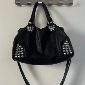 Svart väska med nitar  - Snygg svart väska med nitar. Jag har köpt den second hand så därför vet jag inte vart den är ifrån. 