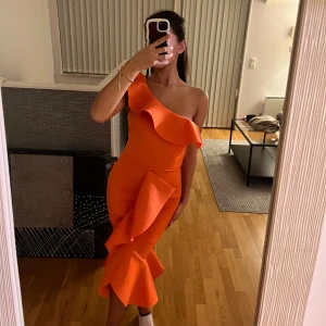 Festklänning - En ursnygg orange festklänning med volanger som detalj. Klänningen är figursydd så den sätter sig perfekt efter ens kroppsform. Den är använd endast en gång! Den är i storlek S men kan även passa andra storlekar då den är strech!💗