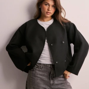 Svart kort kappa  - En helt ny svart kort kappa ifrån Gina Tricot men beställd från Nelly. Super snygg och bra kvalitet aldrig använd. Prislappar sitter kvar och förpackningen finns. Är en storlek xs men passar en S. Perfekt till hösten! 