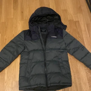 Grå och svart pufferjacka från Everest - Säljer en snygg och varm pufferjacka från Everest i mörkt grönt och svart. Jackan har en praktisk huva och dragkedja framtill. Perfekt för kalla vinterdagar! 🖤 Strolek: 158/164 
