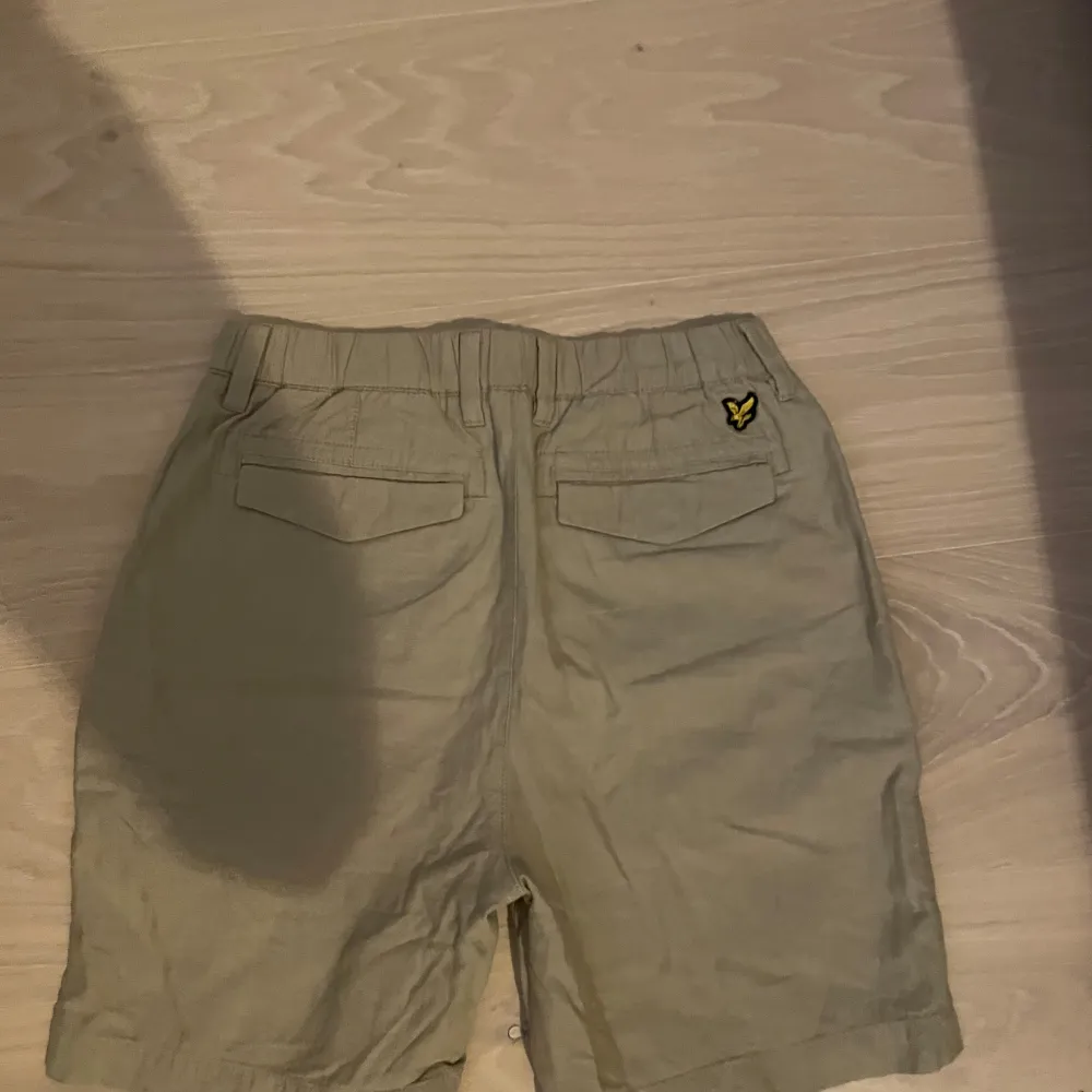 Säljer ett par snygga beige shorts från Lyle & Scott. De har en klassisk design med knapp och dragkedja framtill. Två fickor bak med en liten logga på ena sidan. Perfekta för sommaren!. Shorts.