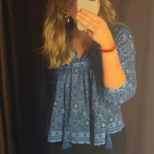 Blå mönstrad blus - Säljer en superfin blå blus med ett unikt mönster. Den har trekvartsärmar och en lös passform som gör den perfekt för både vardag och fest. Blusen är i ett mjukt och bekvämt material.