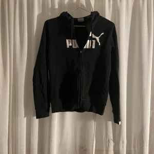 Svart hoodie från Puma - Säljer en svart hoodie från Puma i storlek S. Den har en dragkedja framtill och en stor Puma-logga i vitt på bröstet. Perfekt för en casual look eller träning. Den är i bra skick och superbekväm!
