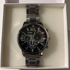 Silverfärgad klocka från Beyros - Säljer en snygg och stilren klocka från Deyros. Den har en silverfärgad metallarmband och en svart urtavla med flera små urtavlor för extra funktioner. Perfekt för både vardag och fest! Vid snabb affär skickas även ett stilrent silverfärgat armband.