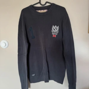 Svart tröja från Morris - Säljer en snygg svart tröja från Morris med broderad logga och nummerdetalj på bröstet. Tröjan är i bra skick och har långa ärmar. Perfekt för både vardag och lite finare tillfällen. Passar bra till jeans eller chinos!