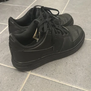 Svarta Nike sneakers - Säljer ett par svarta Nike Air Force. De har en klassisk design med snörning och är perfekta för vardagsbruk. 