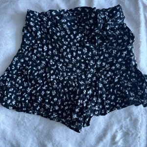 Kort blommig kjol - Kort ”kjol” med inbyggda shorts. Strl M men sitter som S. Svart med vita blommor, perfekt till sommaren. Skriv för fler bilder! 💛 