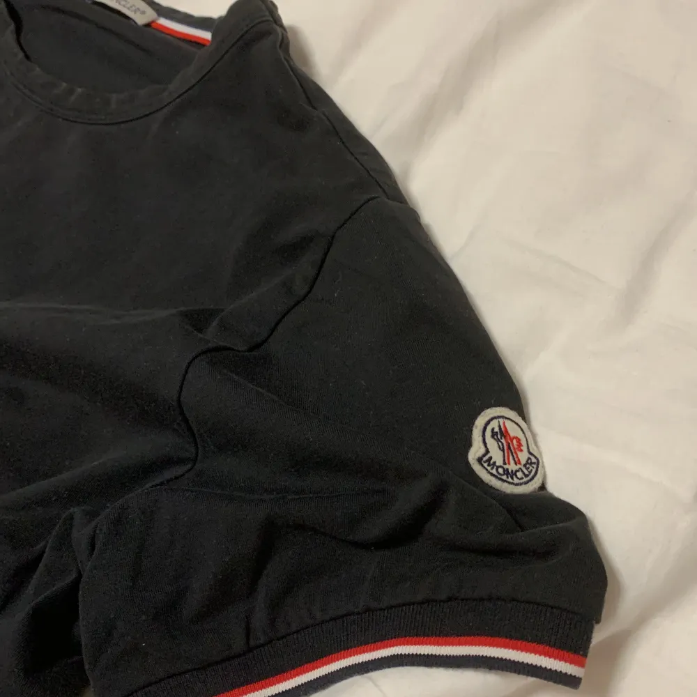 Säljer en snygg svart t-shirt från Moncler. Den har korta ärmar med en cool randig detalj i rött och vitt vid ärmsluten. Använder den inte längre. Väldigt skön och bra passform.. T-shirts.