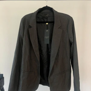 GRÅ KAVAJ - Grå randig kavaj med axelvaddering. Kavajen är en del av ett set med en kjol. Prislappen sitter kvar. Från soyaconcepts premium kollektion. Nypris 1099kr.