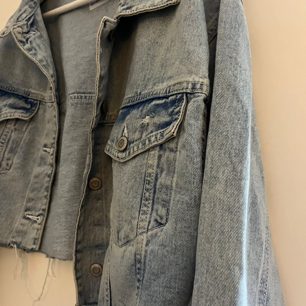 Säljer en snygg jeansjacka från Bershka i storlek M. Den är i en klassisk blå denimfärg och har en croppad stil med slitna detaljer för en cool look. Jackan har knappar framtill och två bröstfickor med knappstängning. Perfekt för vår och sommar!. Jackor.