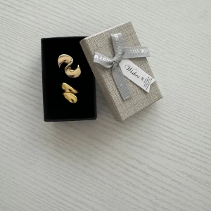 Guld ringar i elegant design - Säljer ett par snygga ringar med en modern och stilren design. De kommer i en fin presentask med en söt rosett, perfekt som gåva eller för att skämma bort dig själv.Ringar har en mjuk, böjd form som ger en elegant touch till vilken outfit so