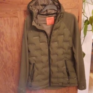 Olivgrön pufferjacka från Superdry - Säljer en snygg olivgrön pufferjacka från Superdry i storlek medium. Jackan har en quiltad design med dragkedja och huva, perfekt för kyliga höst- och vinterdagar. Den är i bra skick och har en normal passform. Perfekt för dig som vill hålla stilen samtidigt som du håller dig varm!