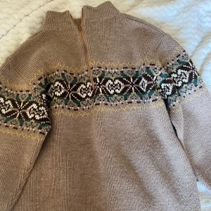 Beige stickad tröja med mönster - Säljer en supermysig beige stickad tröja med ett snyggt mönster i brunt, grönt och vitt. Tröjan har en dragkedja vid halsen och långa ärmar. Perfekt för kalla höst- och vinterdagar!Står ingen storlek men skulle säga att den passar s&m