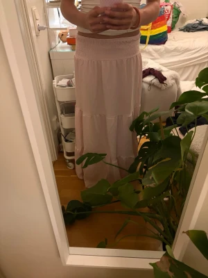 Ljusrosa långkjol från 157 - Säljer en ljusrosa långkjol från 157 i storlek XS. Kjolen har en smockad midja och faller snyggt i ett mjukt, tunt tyg. Perfekt för varma dagar och enkel att styla med både toppar och sneakers.