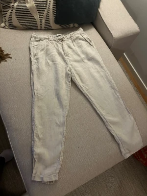 Beiga linnebyxor från Zara - Snygga beiga linnebyxor från Zara i storlek 38. Byxorna har raka ben, fickor på sidorna och stängs med knapp och dragkedja. Perfekta för en avslappnad och trendig look. Tillverkade i ett luftigt linnematerial.
