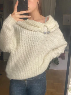 Vit fluffig stickad tröja med krage - Mysig vit stickad tröja i fluffigt material med bred krage och dekorativa knappar. Tröjan har en avslappnad passform och långa ärmar, perfekt för kalla dagar. Passar till jeans eller kjol för en chill look.
