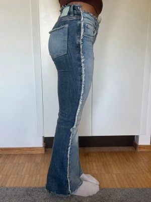 Tvåfärgade bootcut jeans med råa kanter - Unika bootcut jeans i två olika blå tvättar med råa, fransiga kanter längs sidorna. Låg midja och klassisk femficksmodell. Jeansen har en cool kontrast mellan fram- och baksida och är tillverkade i denim med stretch.