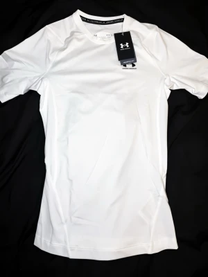 Under Armour compression  - Snygg vit kortärmad träningströja från Under Armour med rund hals och diskret logga på bröstet. Tillverkad i ett lätt och stretchigt funktionsmaterial som andas, perfekt för intensiva träningspass eller löpning.