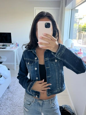 Mörkblå klassisk jeansjacka - Snygg mörkblå jeansjacka med silverfärgade knappar och två bröstfickor från märket Reserved! Jackan har en klassisk rak passform och kontrastsömmar som ger en tidlös look. Perfekt att slänga över en topp för en avslappnad stil.