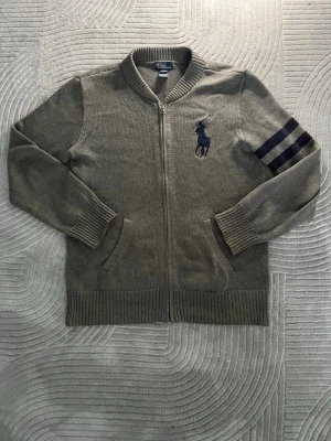 Ralph lauren cardigan tröja - Halloj halloj! Säljer min gråa Ralph Lauren cardigan/tröja eftersom den är lite för liten för mig. Den är i storlek L men passar som M. Tröjan är i fantastiskt skick, den två klassiska ränderna på vänster ärm och stora loggan fram på vänster bröst. Perfekt tröja till dem flesta temperaturer och väder. Tvär snygg tröja om du frågar mig och gör nästan lite ont i hjärtat att sälja den. För mer info så är det bara att skriva 👍👍