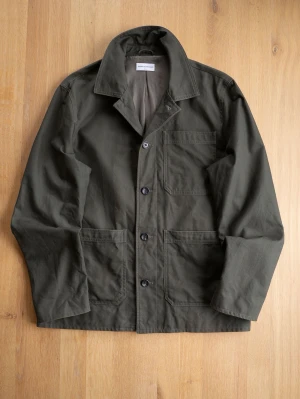 Olivgrön overshirt från These Glory Days - Stilren olivgrön overshirt från These Glory Days med tre utanpåliggande fickor och klassisk krage. Tillverkad i ett tåligt bomullstyg och stängs med fyra knappar framtill. Perfekt lager-på-lager-plagg för en avslappnad look.
