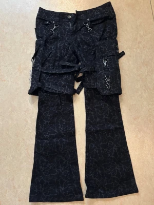 Spräckliga Gothicana jeans med avtagbara fickor - Svarta Gothicana jeans med spräckligt mönster och avtagbara fickor med metalldetaljer.